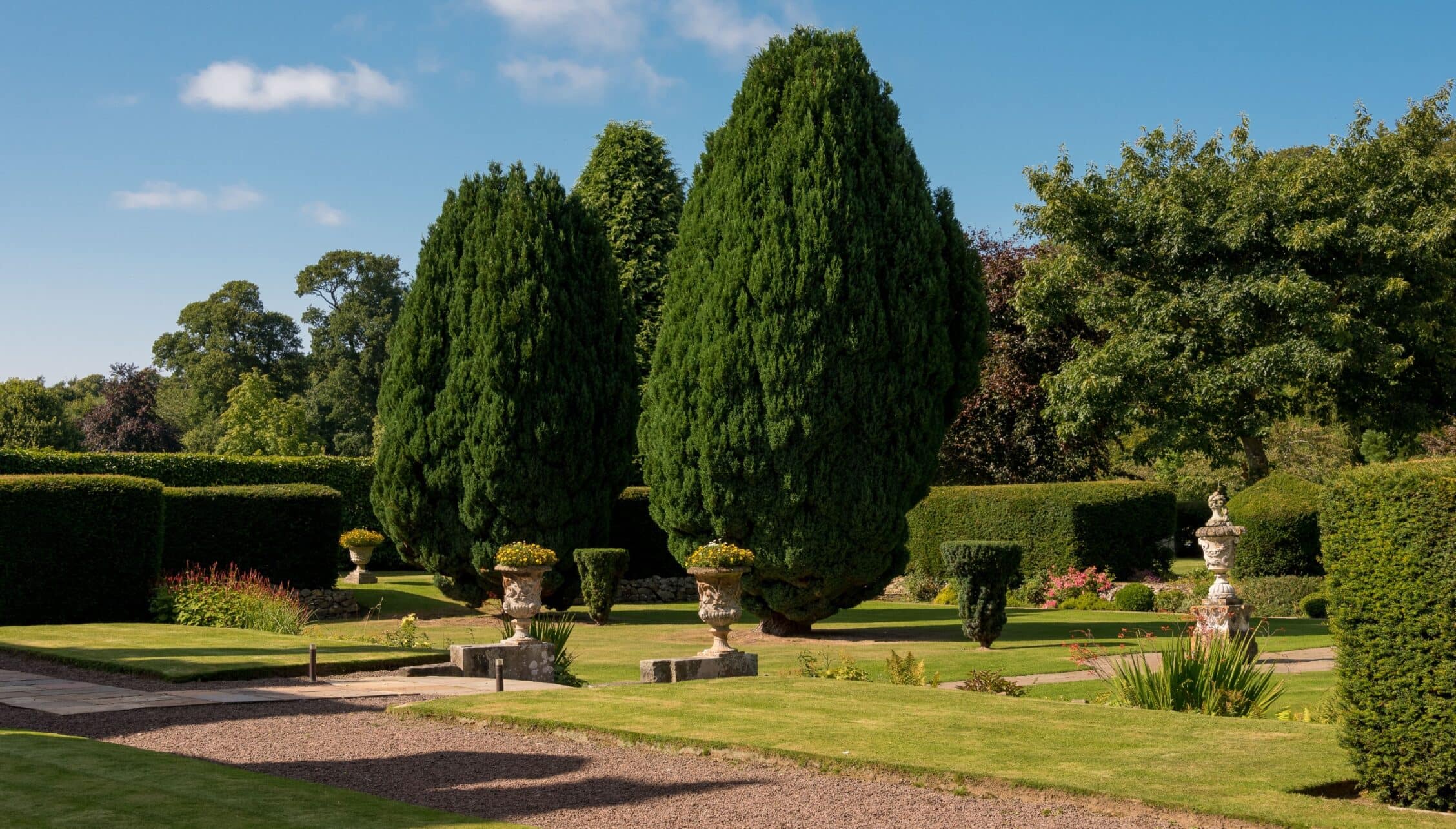 Gilmerton House, East Lothian – Formal gardens with tall conifer trees, stone urns and manicured hedges.