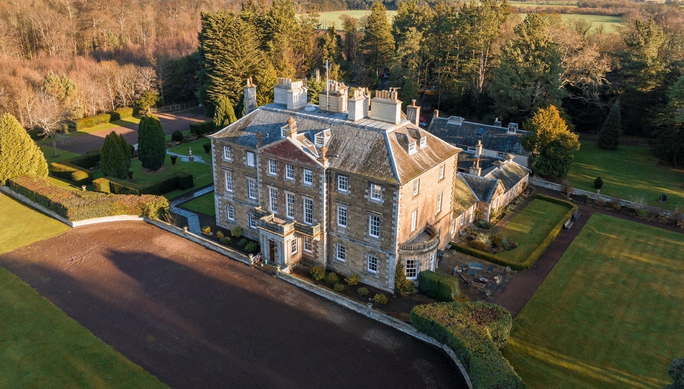 Gilmerton House, East Lothian – Georgian stone mansion with formal grounds, driveway and surrounding woodland in autumn.