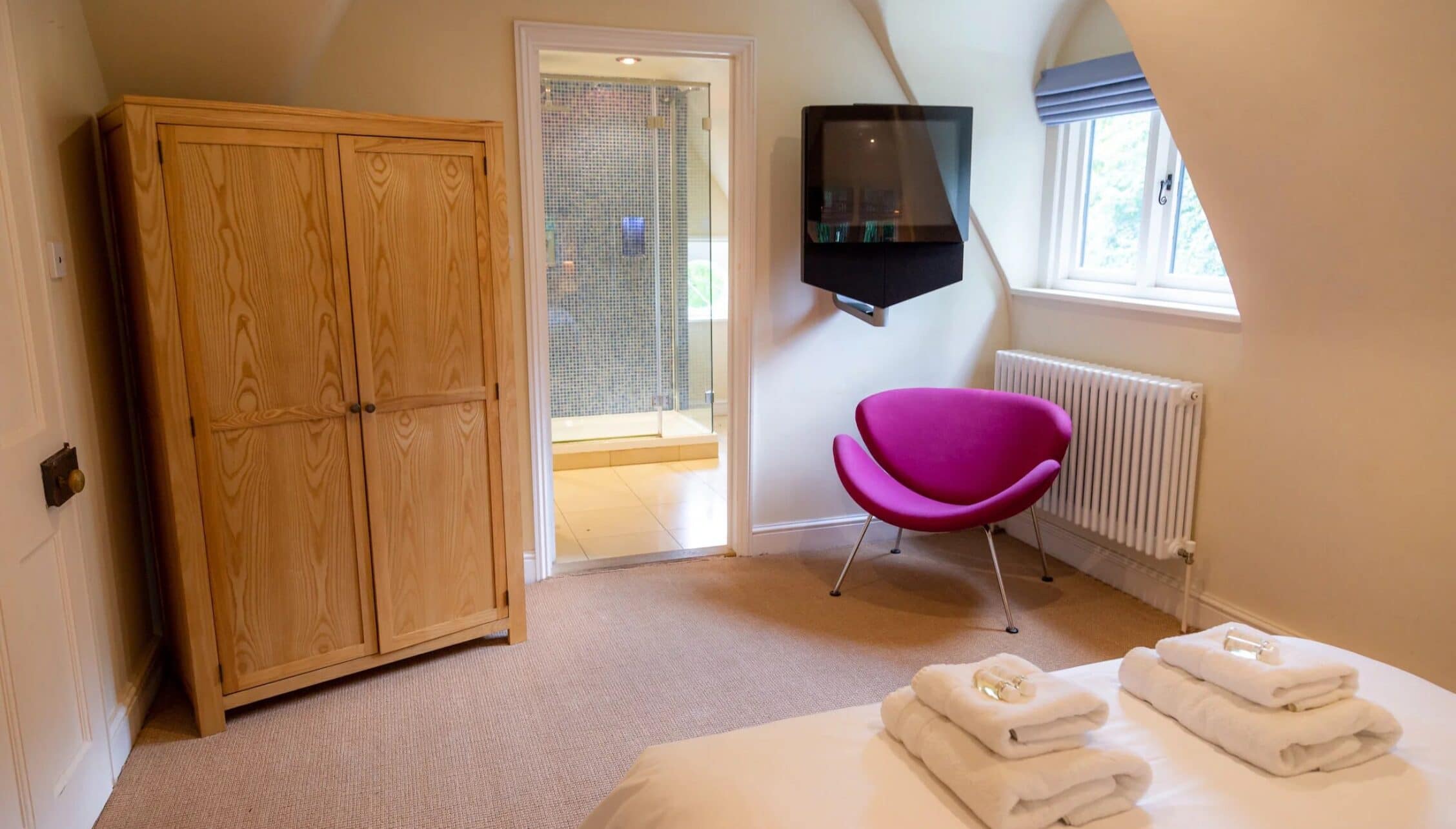 Hill House Norfolk, Norfolk – Bedroom with wooden wardrobe, en-suite shower room, and magenta armchair.