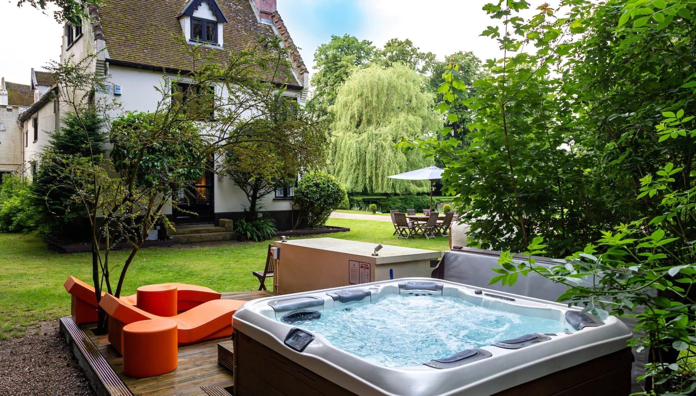 Hill House Norfolk, Norfolk – Hot tub with red seating on decked terrace, country house and manicured gardens beyond.