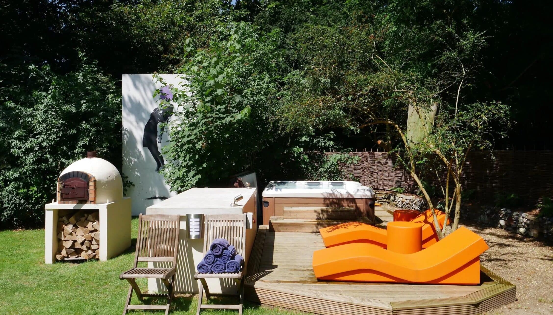 Hill House Norfolk, Norfolk – Garden with hot tub, pizza oven, and orange lounge seating on wooden deck.