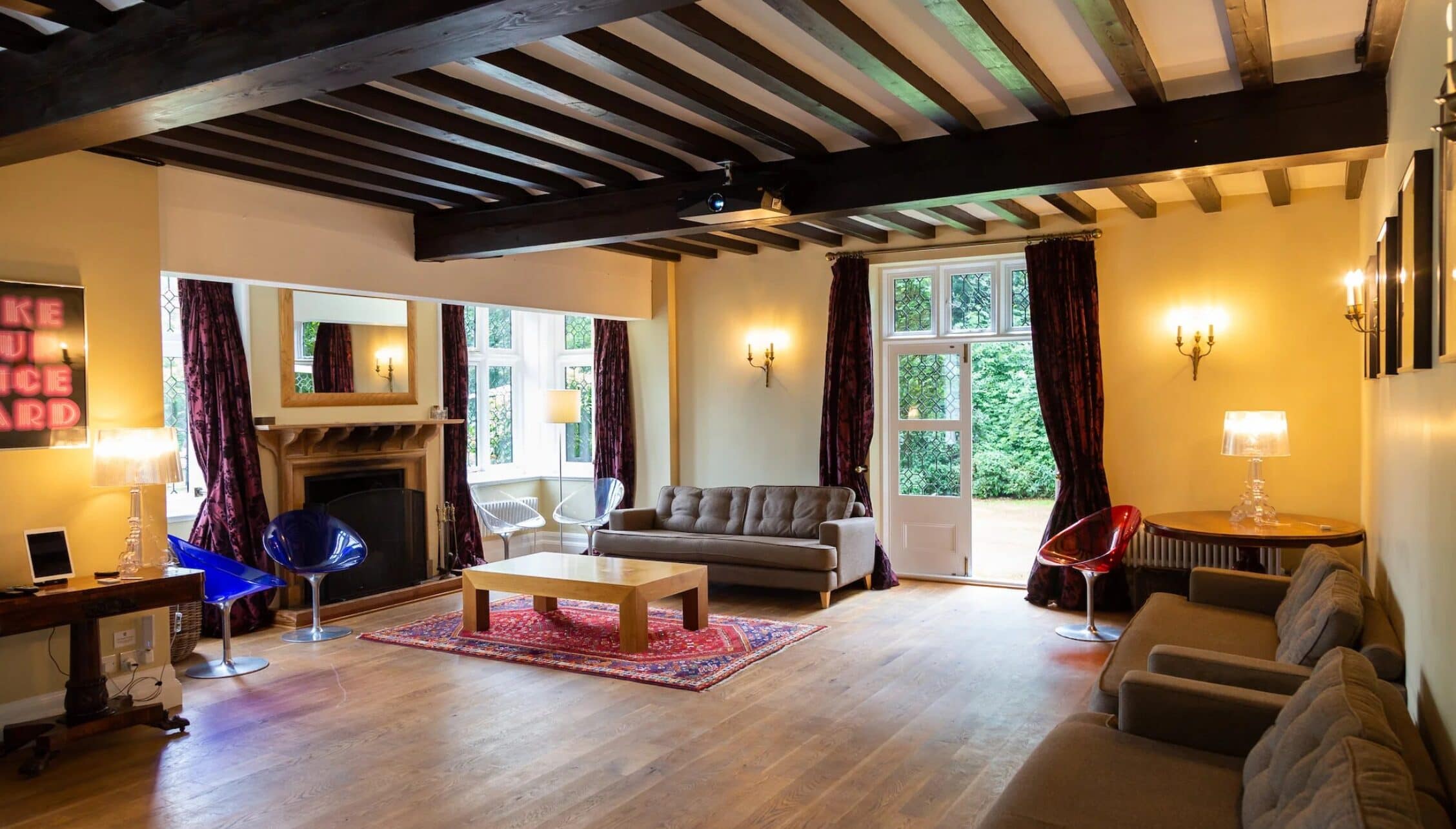 Hill House Norfolk, Norfolk – Spacious living room with exposed wooden beams, fireplace and French doors to garden.