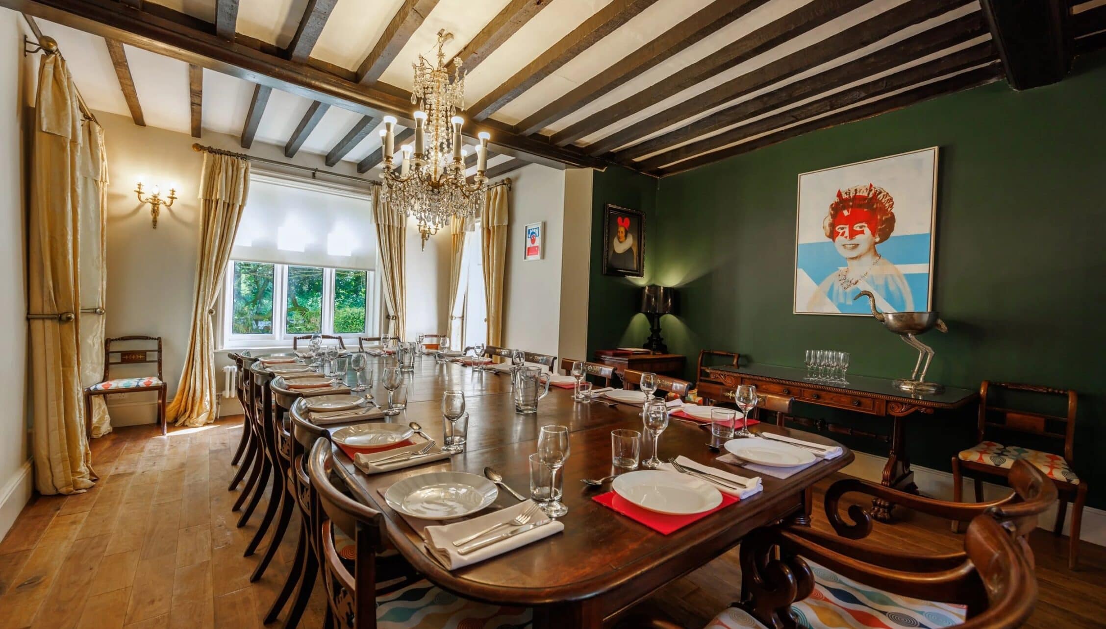 Hill House Norfolk, Norfolk – Dining room with exposed wooden beams, crystal chandelier, and green accent wall.