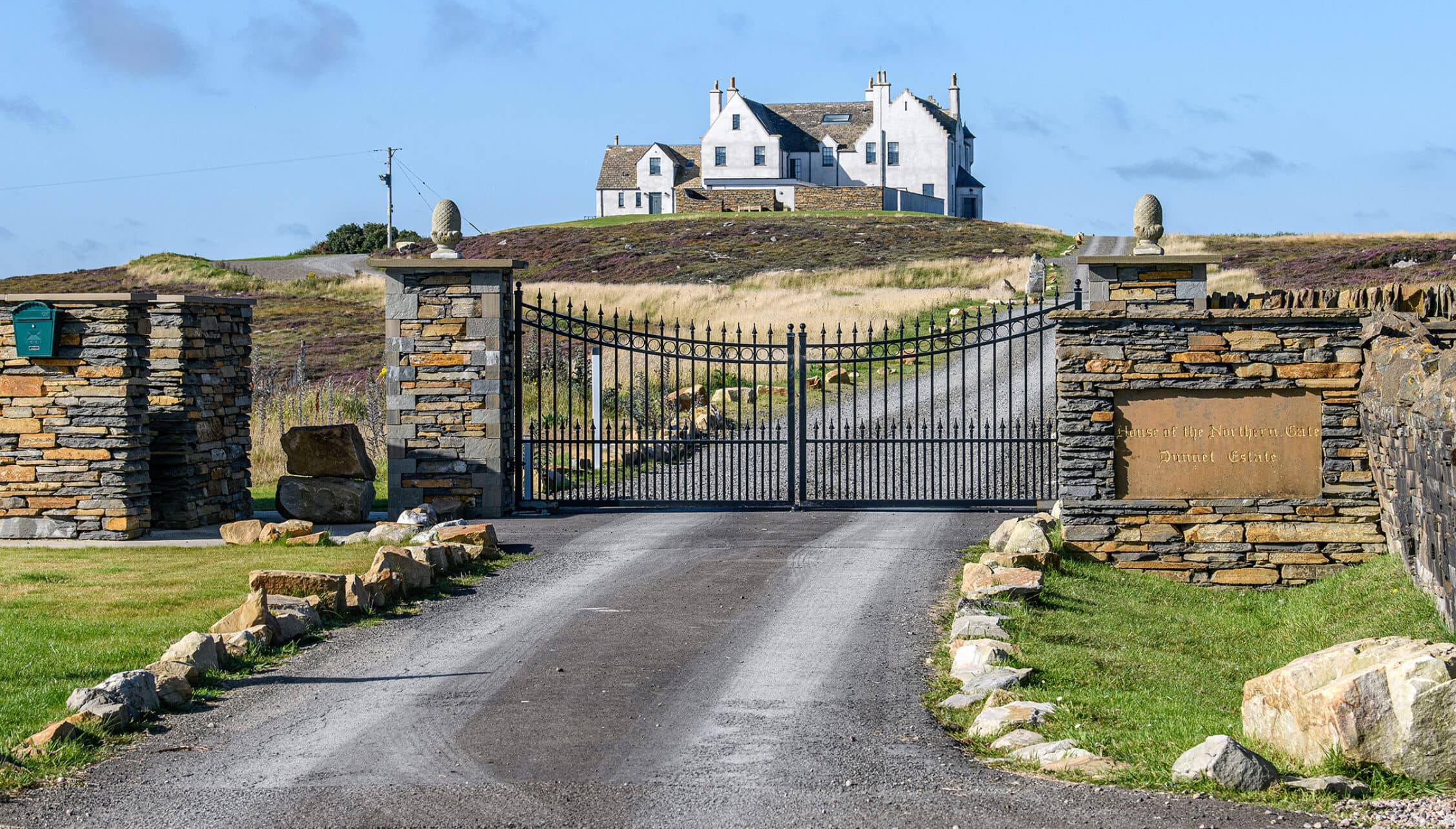 House of the Northern Gate, Highland – White stone country house on moorland hillside with black iron gates and stone gateposts.