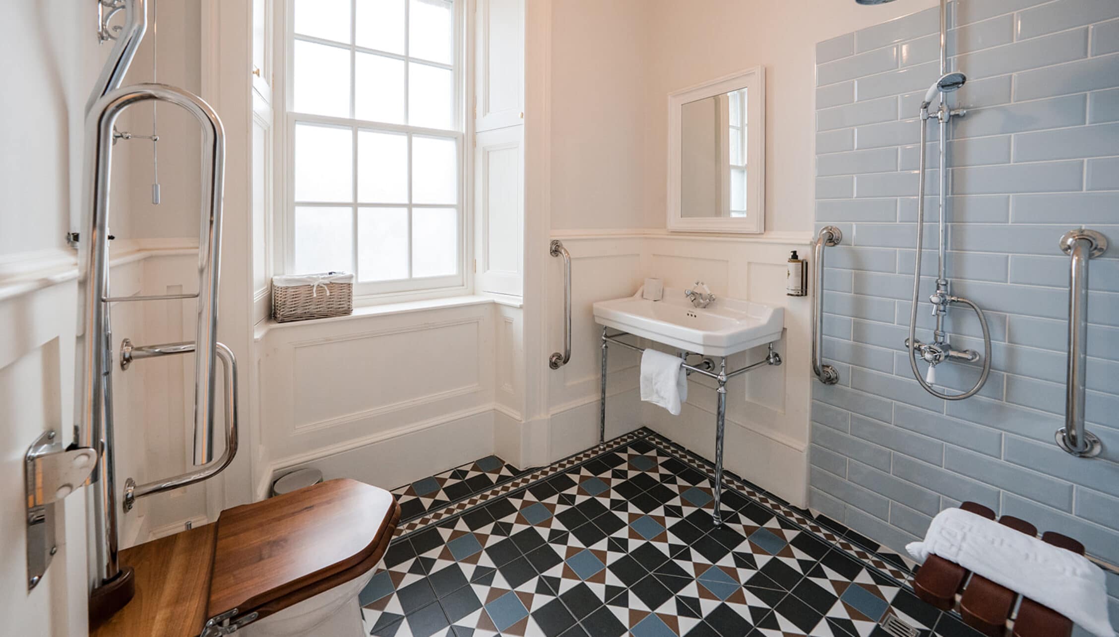 House of the Northern Gate, Highland – Bathroom with black and white geometric floor tiles, blue subway tiling, and pedestal sink.