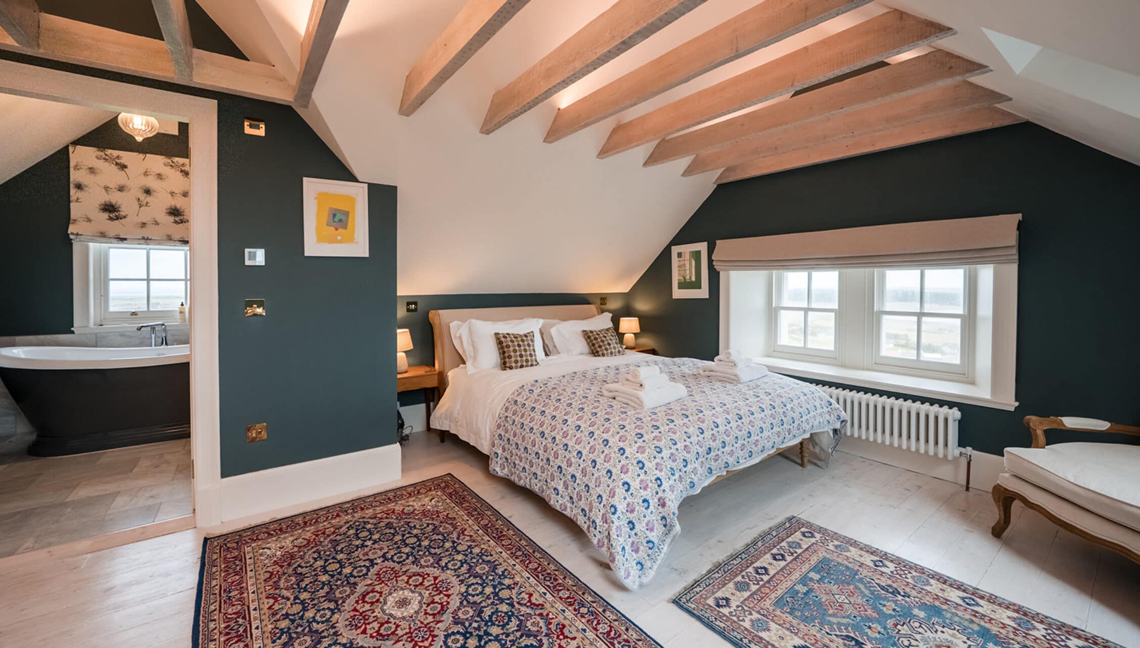 House of the Northern Gate, Highland – Attic bedroom with exposed wooden beams, dark feature wall, and ensuite bathroom.