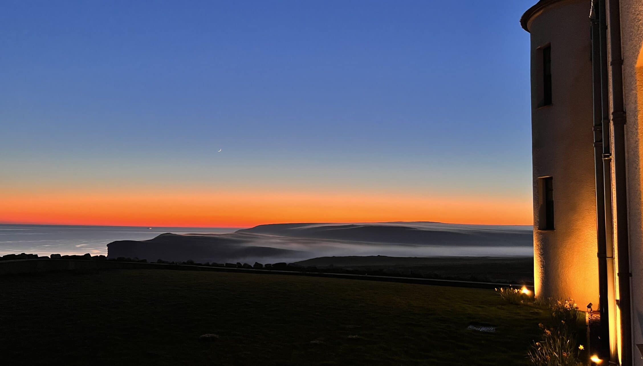 House of the Northern Gate, Highland – Stone tower at sunset overlooking moorland and distant sea.
