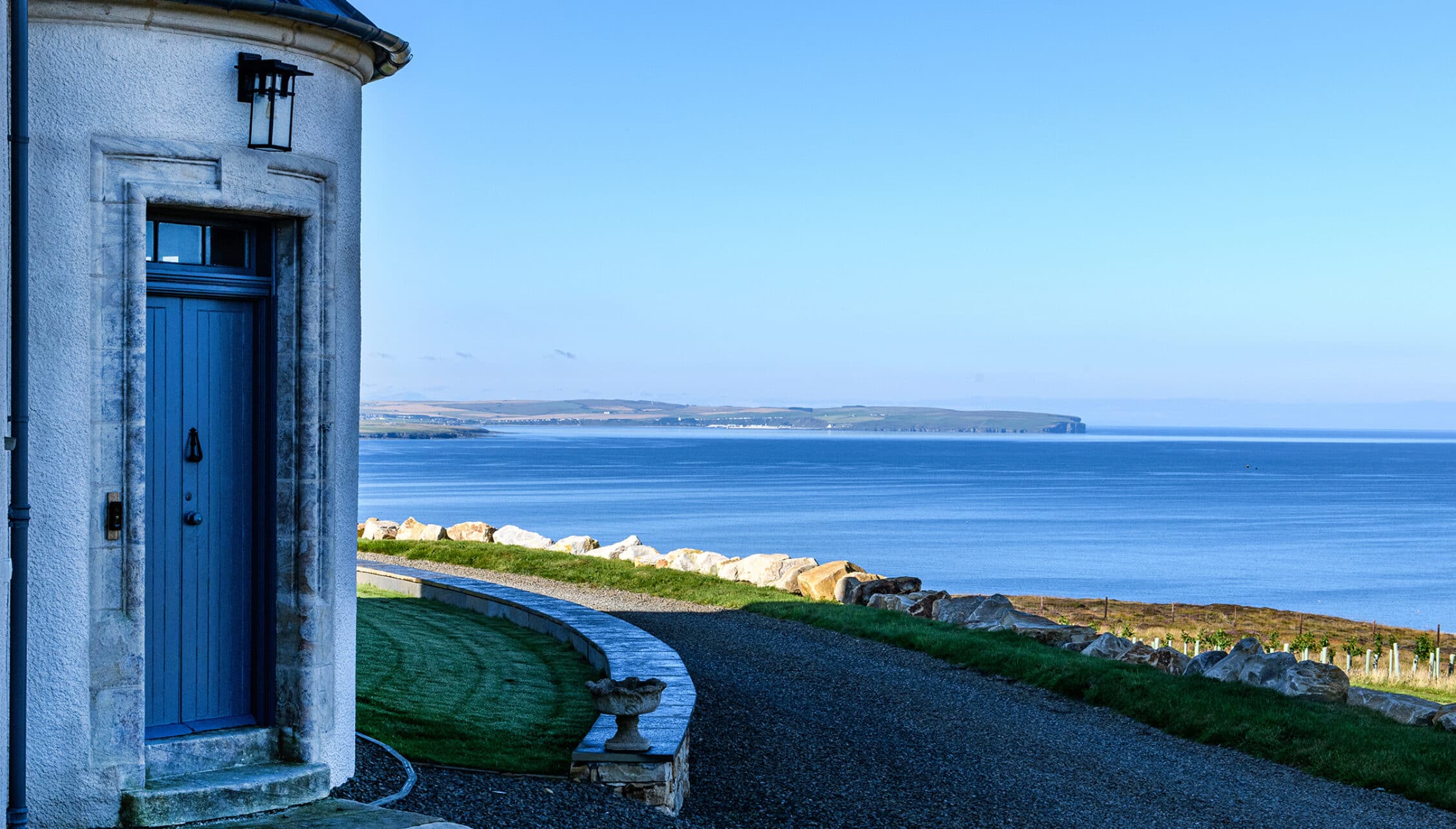 House of the Northern Gate, Highland – Whitewashed cottage with blue door overlooking sea and rocky coastline.