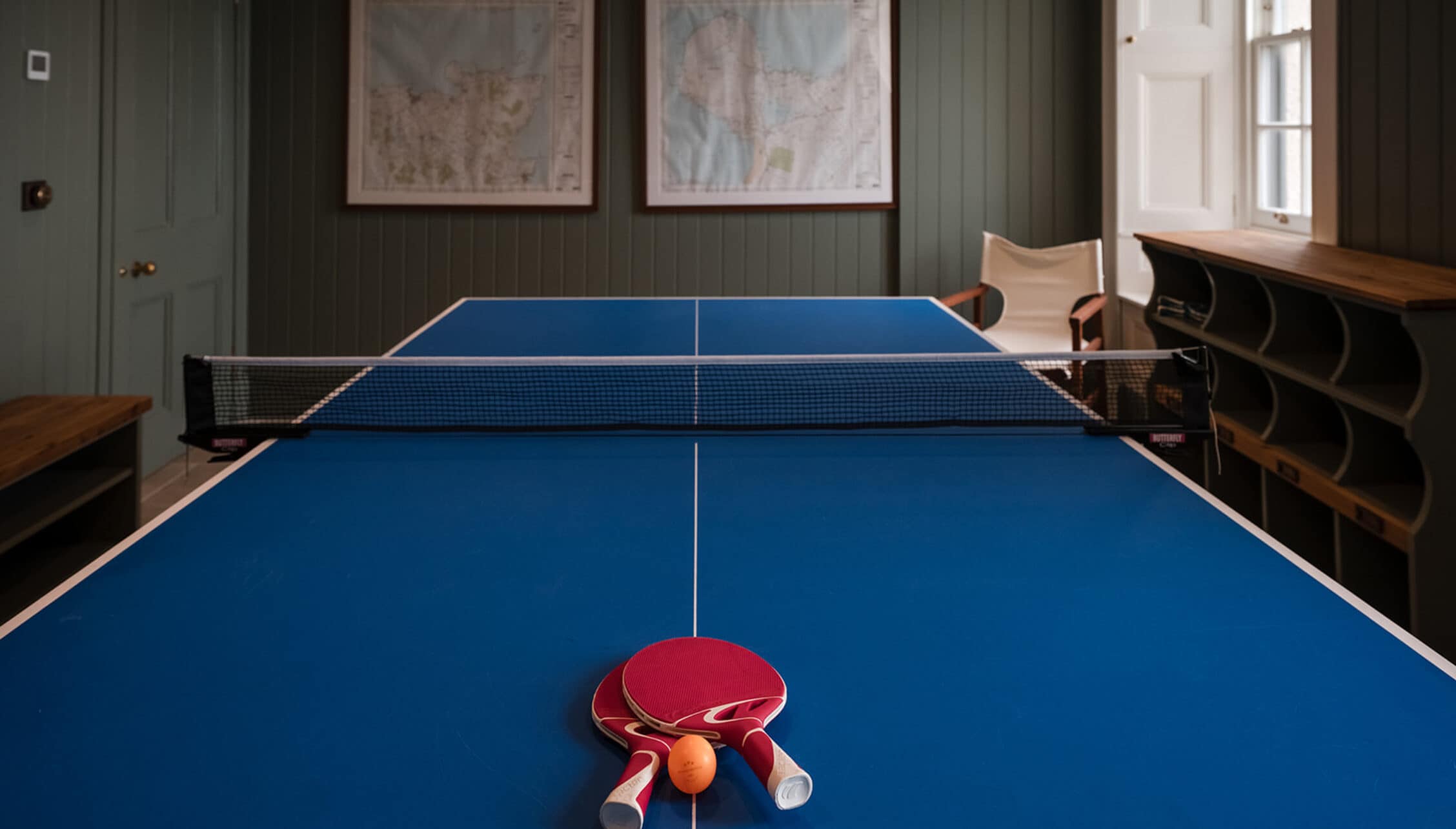 House of the Northern Gate, Highland – Table tennis room with blue playing surface and paddles, sage green panelled walls.