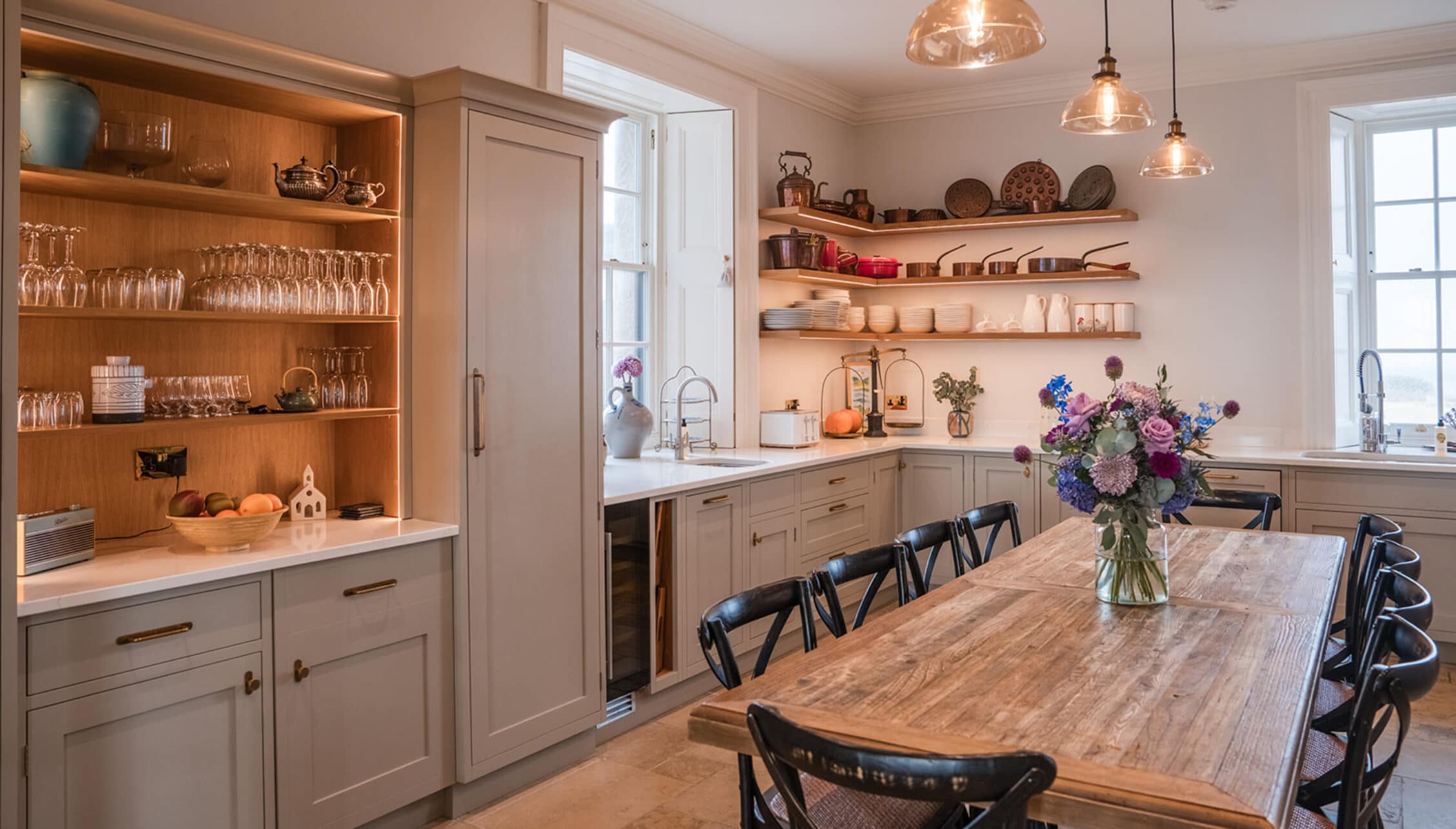 House of the Northern Gate, Highland – Modern kitchen with open wooden shelving, dining table and black chairs beneath copper pendant lights.