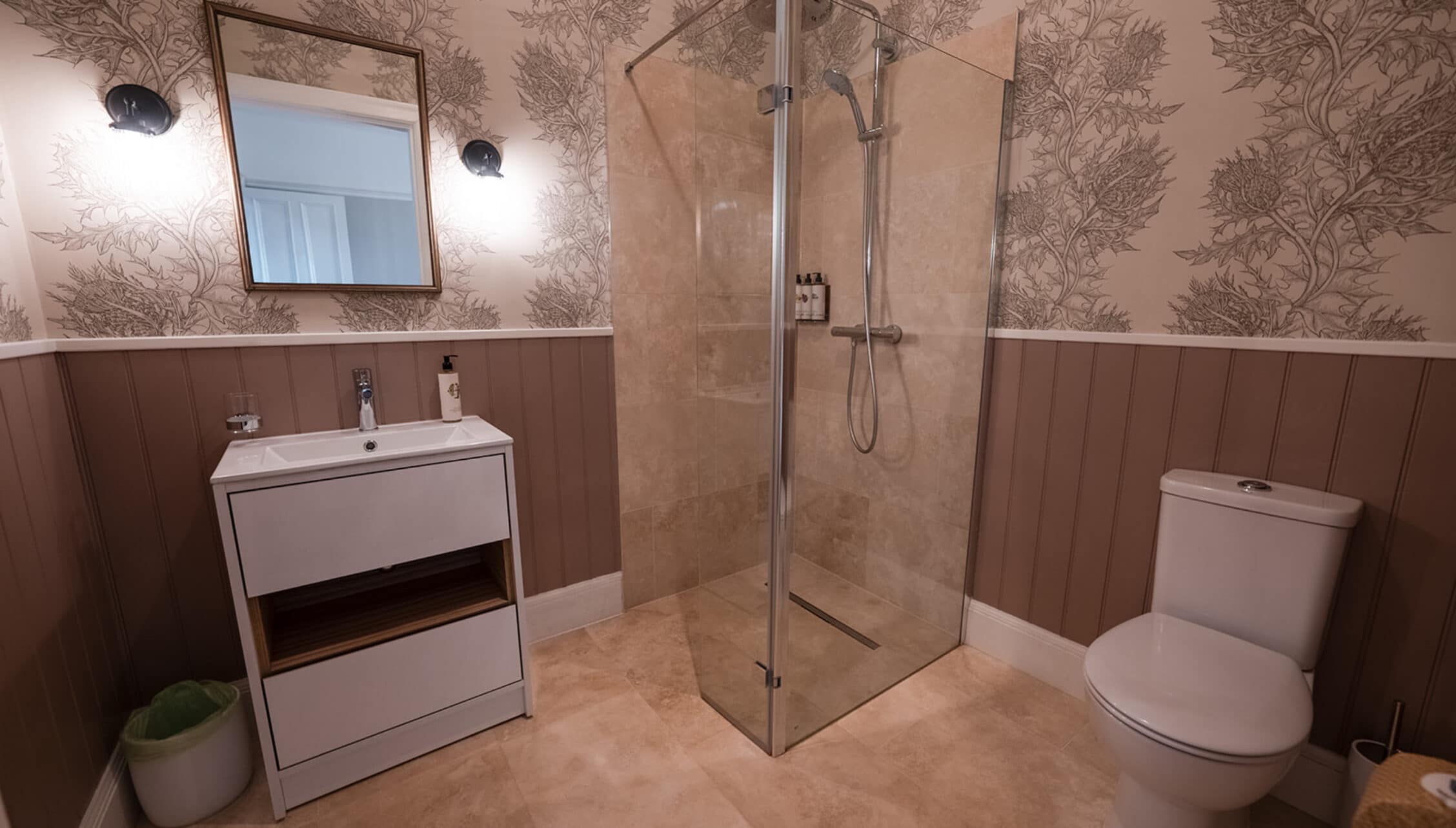 House of the Northern Gate, Highland – Modern bathroom with walk-in shower enclosure, white vanity unit, and botanical wallpaper.