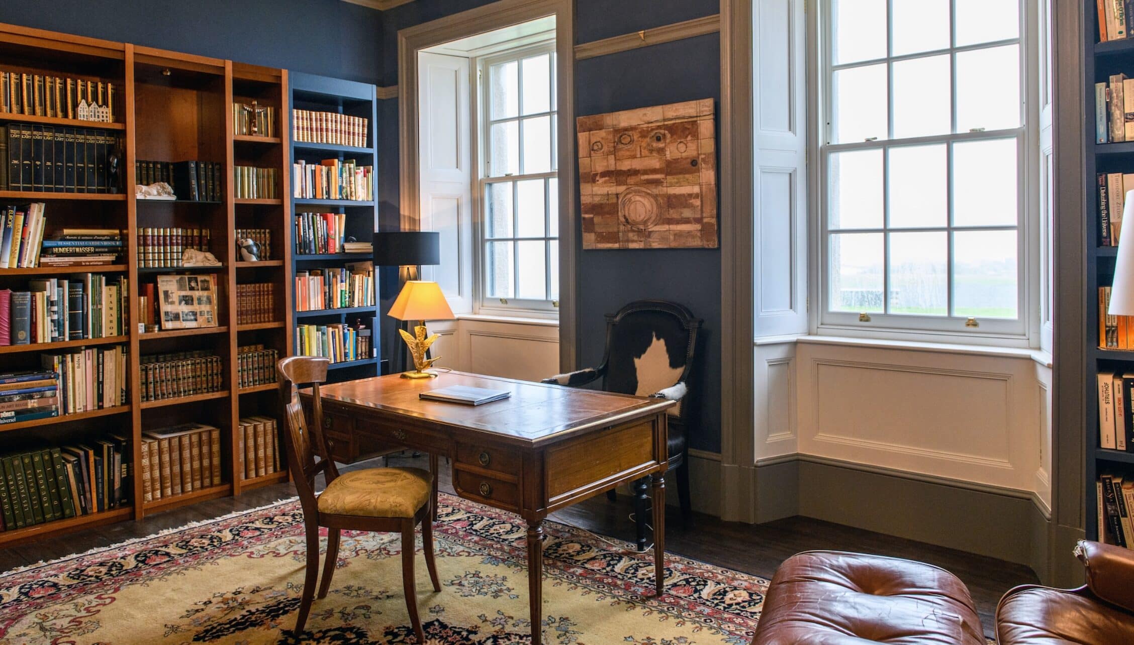 House of the Northern Gate, Highland – Library study with wooden desk, built-in bookshelves, and large sash windows.