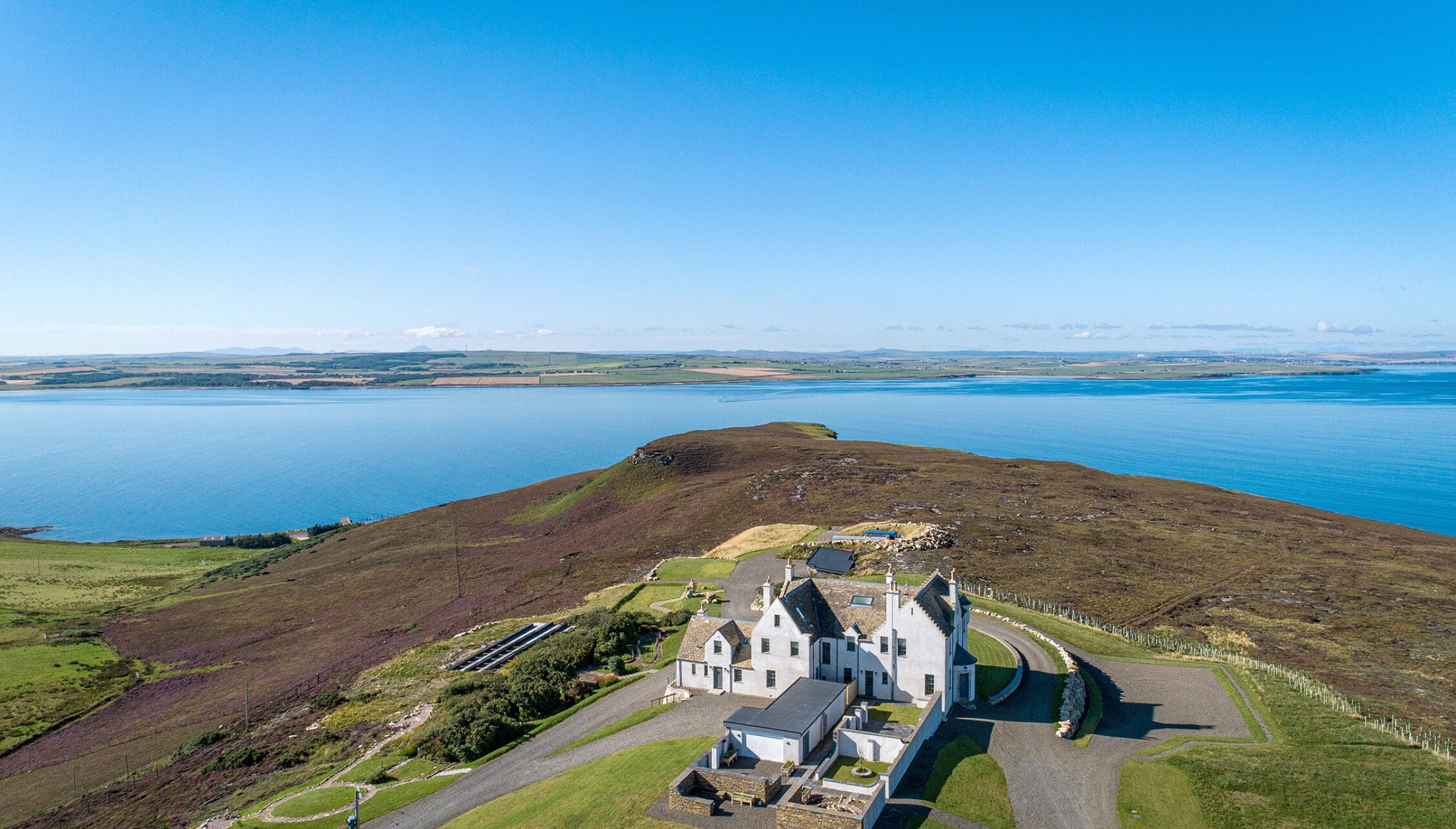 House of the Northern Gate, Highland – White-rendered house on moorland hillside overlooking blue sea and distant farmland.