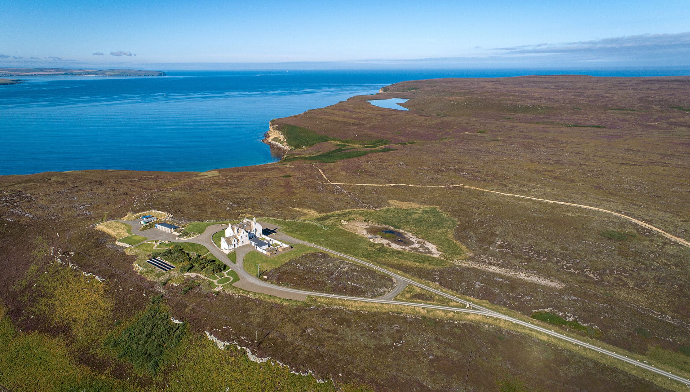 House of the Northern Gate, Highland – Aerial view of white house set on moorland overlooking blue sea and coastal cliffs.