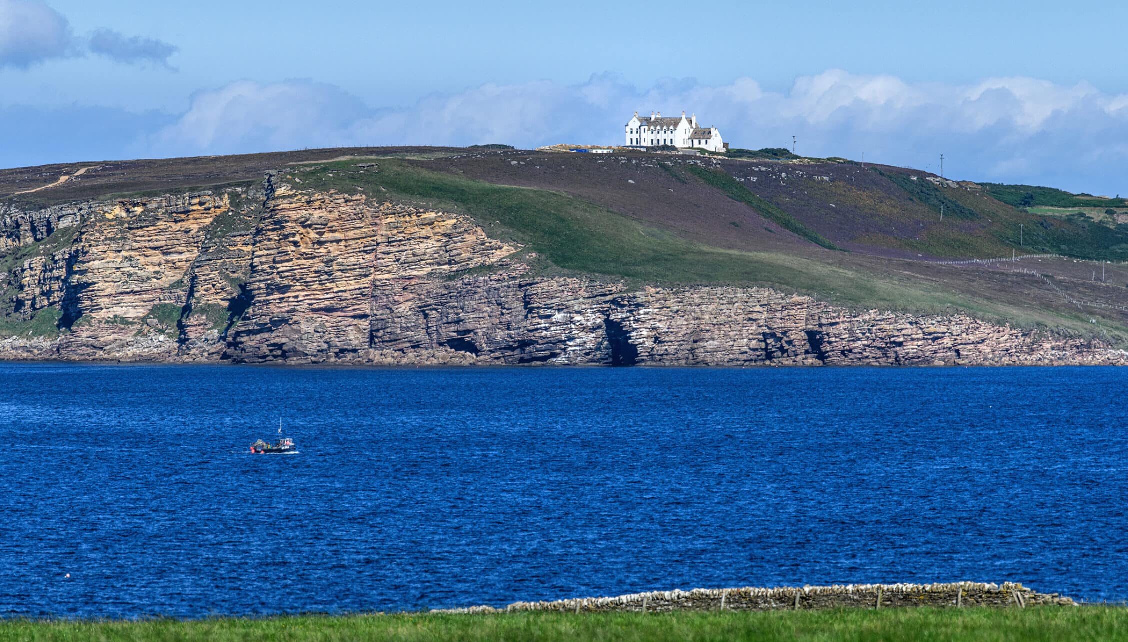 House of the Northern Gate, Highland – White mansion on rocky headland overlooking blue sea and coastal cliffs.