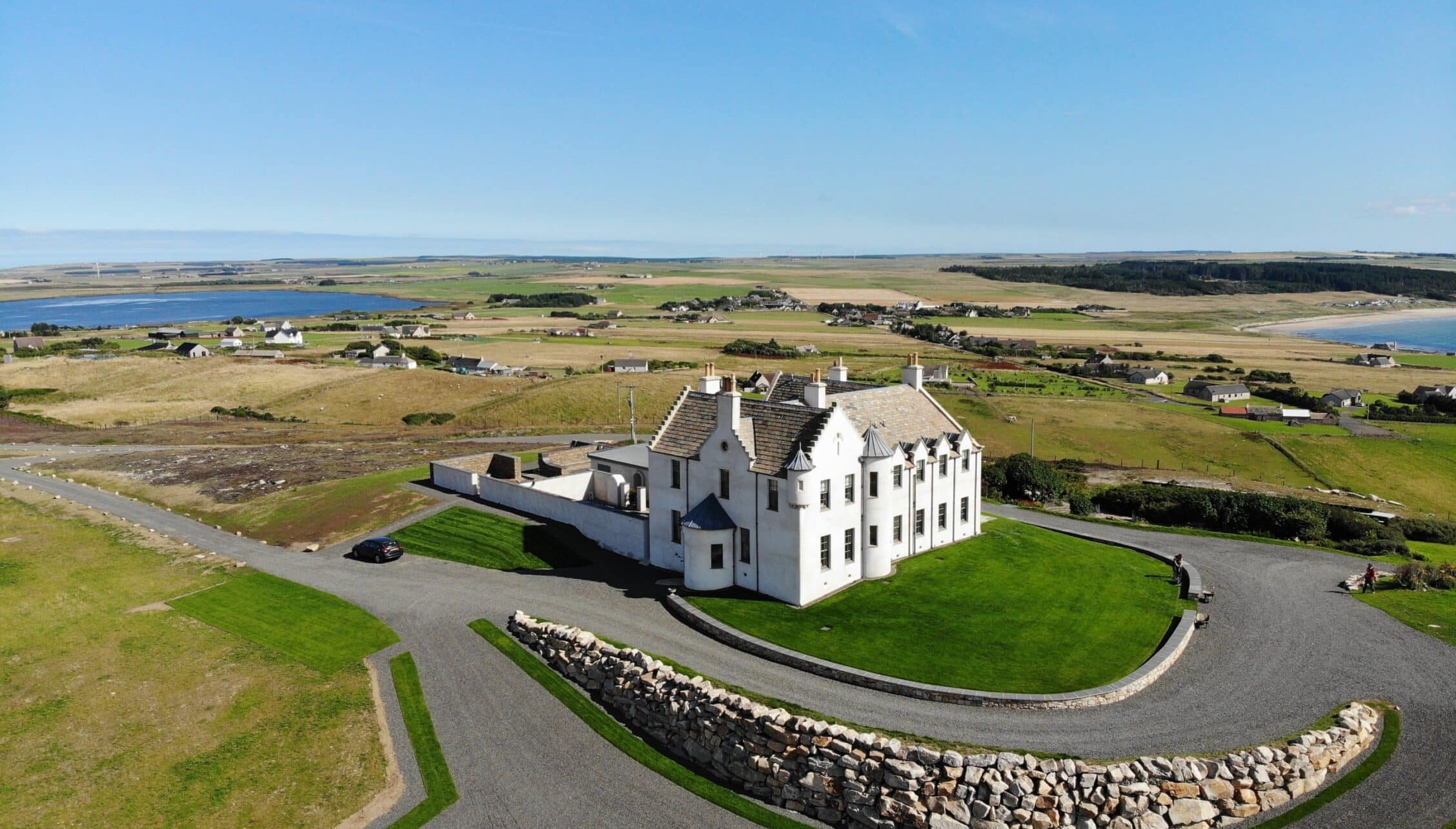 House of the Northern Gate, Highland – White harled house with multiple chimneys set in green grounds overlooking moorland and lochs.