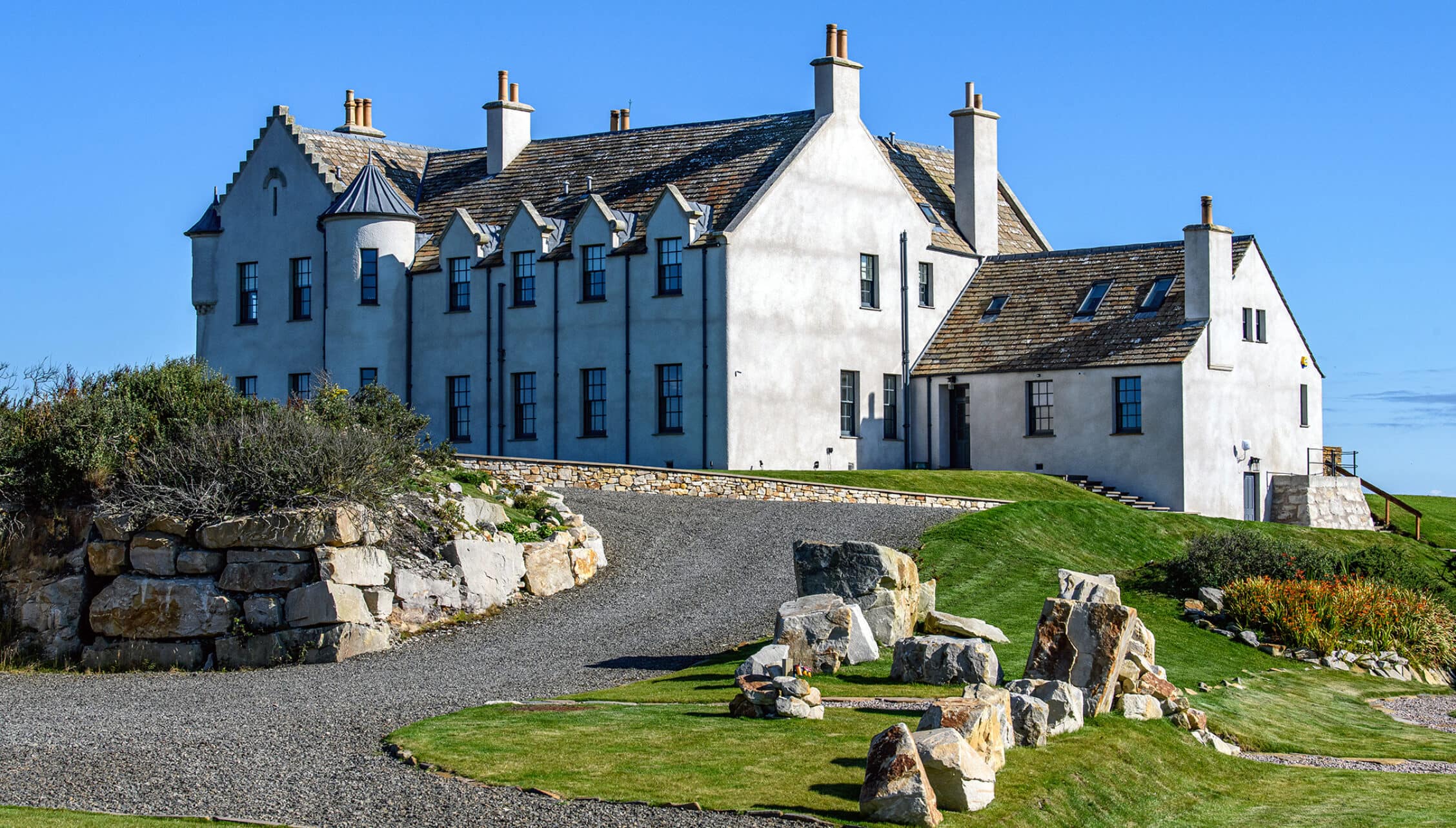 House of the Northern Gate, Highland – White rendered country house with slate roof and stone chimneys on grassy hillside.