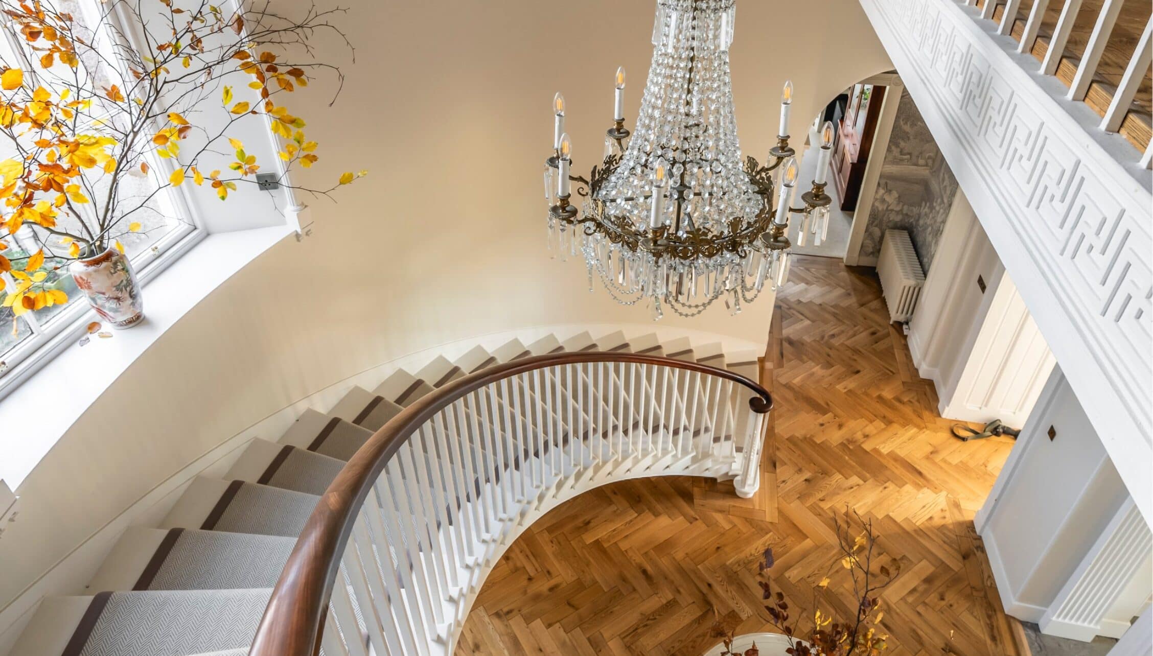 Manar House, Aberdeenshire – Grand staircase with curved wooden handrail, crystal chandelier, and herringbone flooring.
