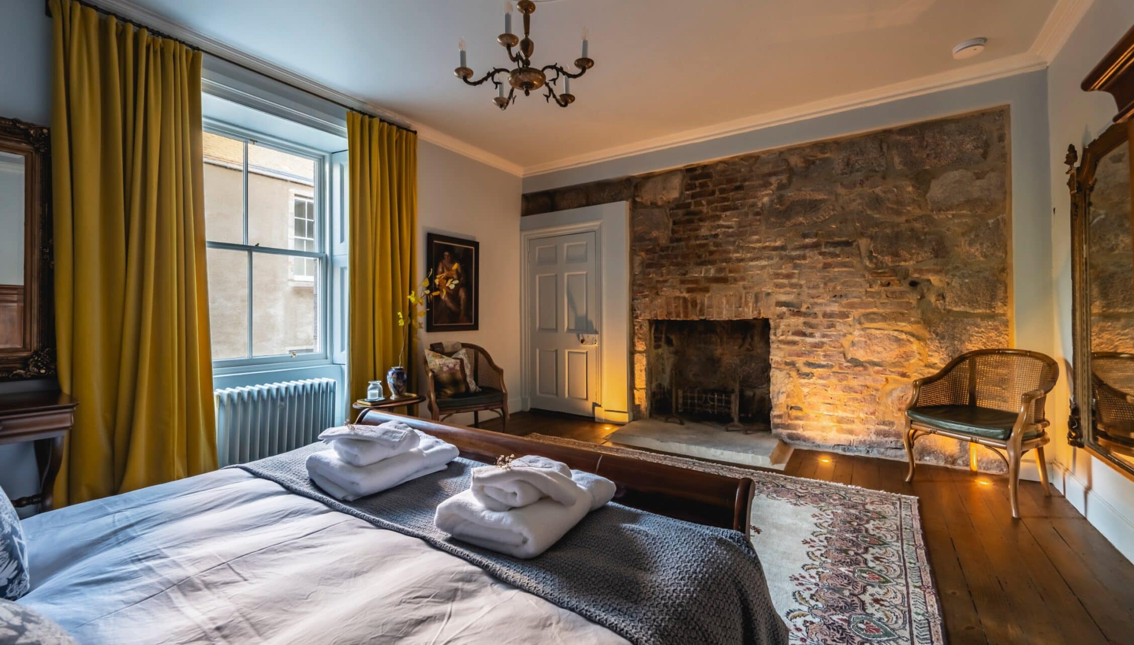 Manar House, Aberdeenshire – Spacious bedroom with exposed brick fireplace, four-poster bed and mustard-yellow curtains.