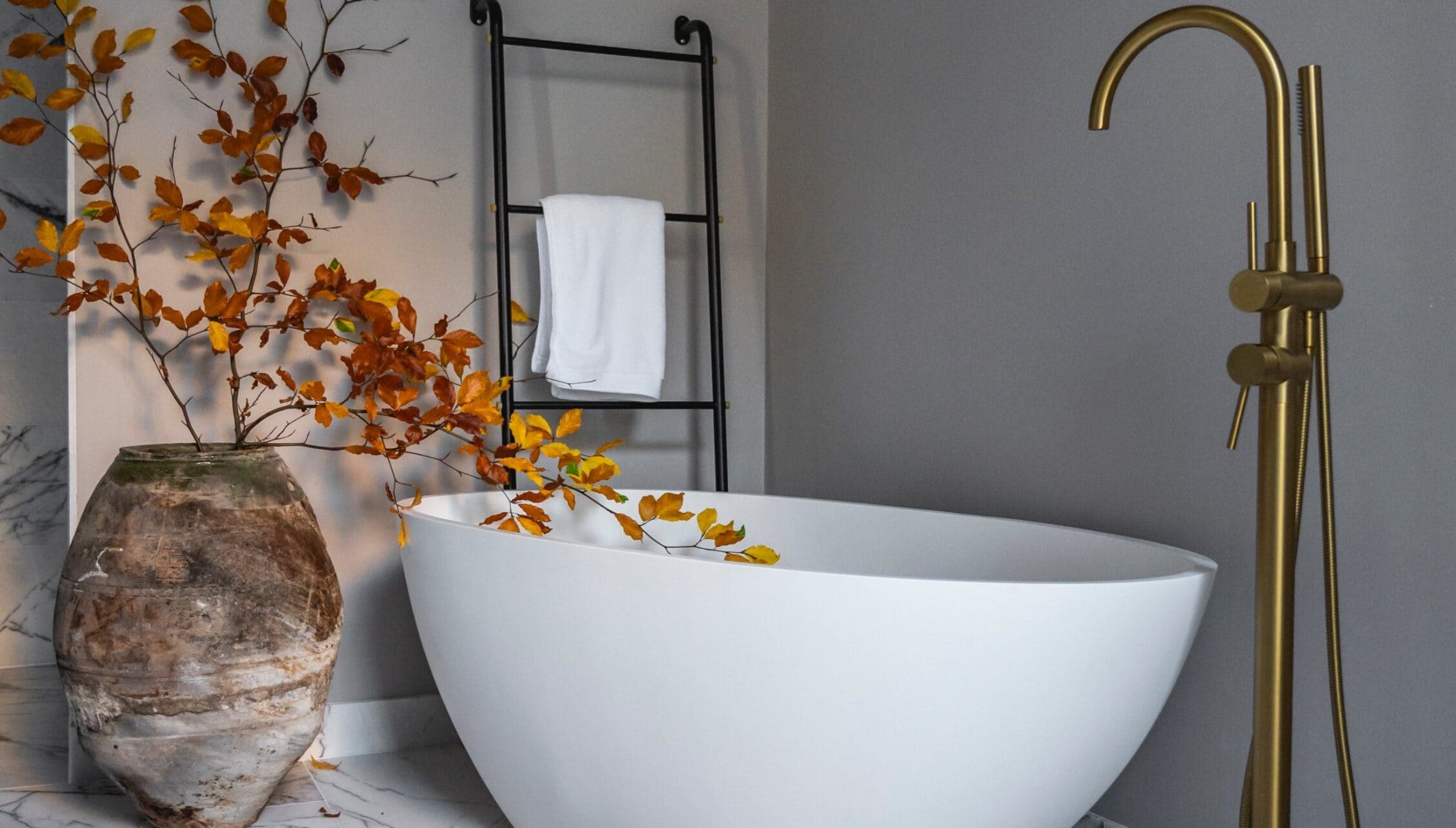 Manar House, Aberdeenshire – White freestanding bath with brass tap, black towel ladder, and dried foliage arrangement.