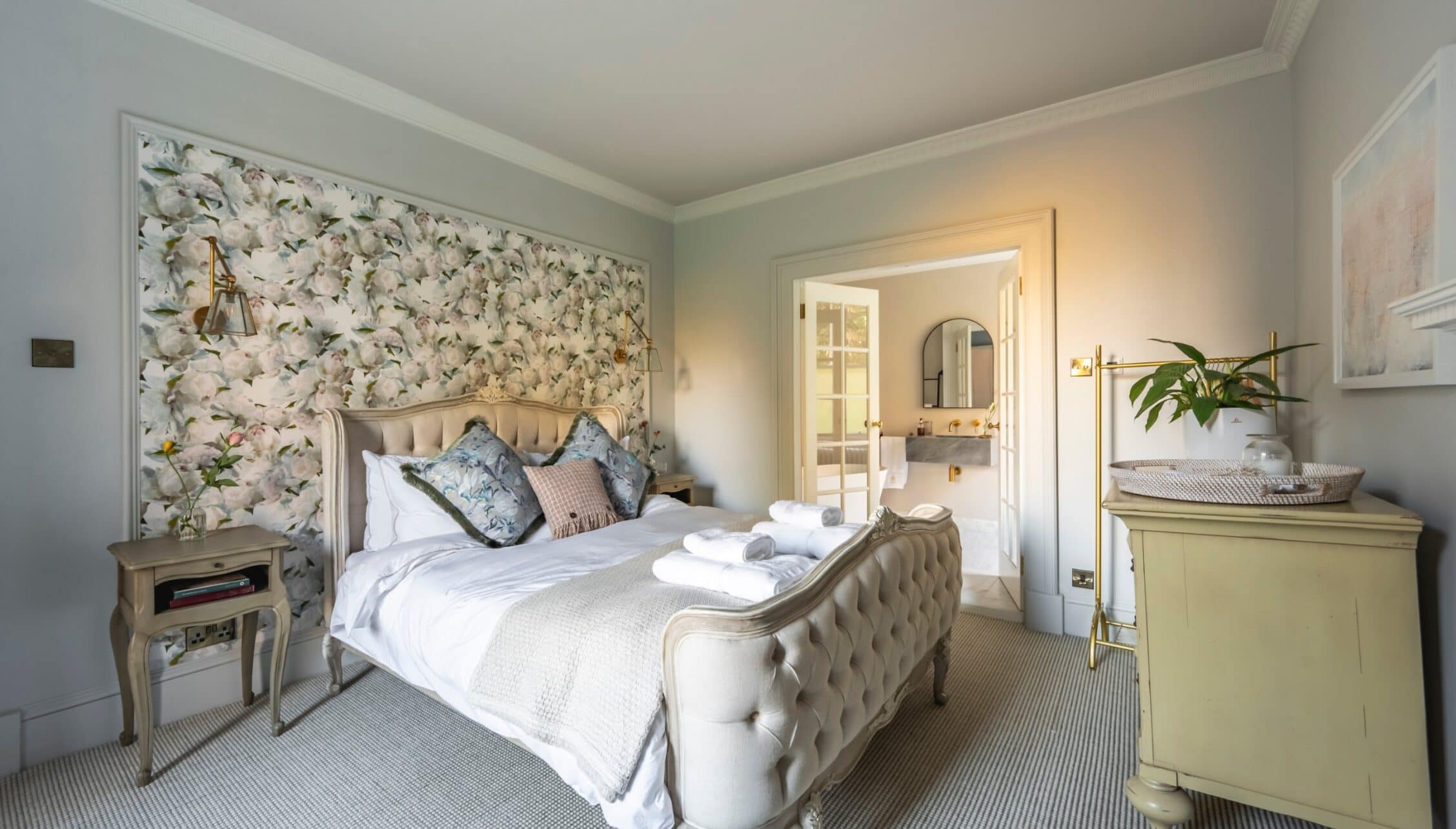 Manar House, Aberdeenshire – Master bedroom with floral headboard wall, en suite bathroom, and cream upholstered bed.