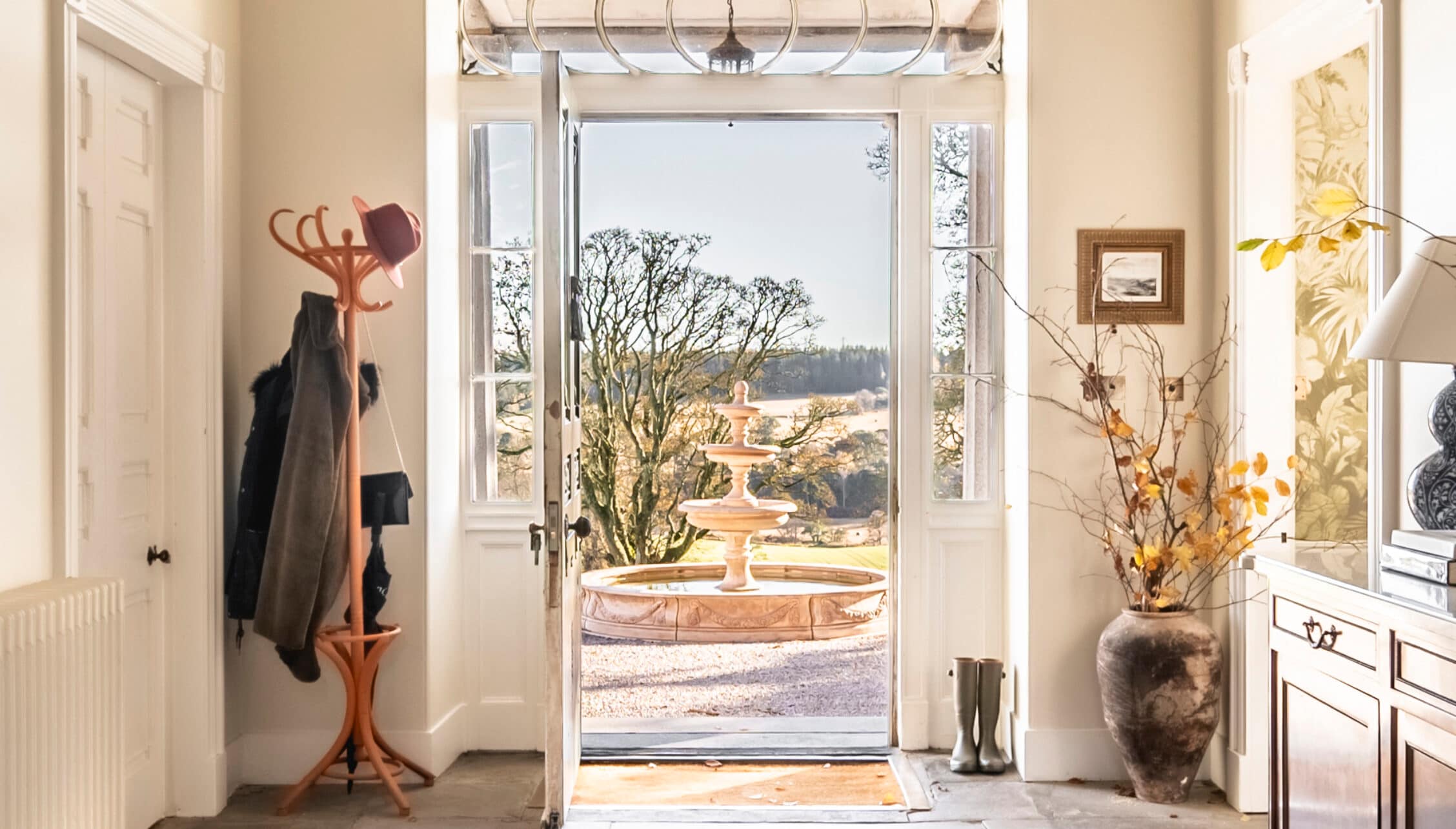 Manar House, Aberdeenshire – Cream hallway with wooden coat stand and open French doors to courtyard with fountain.