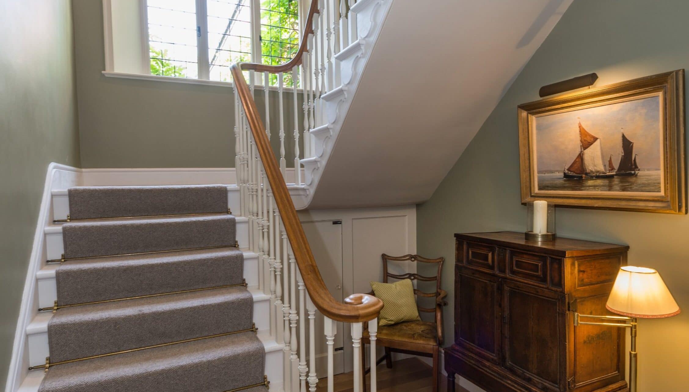Nedging Hall, Suffolk – Staircase with grey carpet runner, wooden banister, and first-floor landing with artwork and furniture.