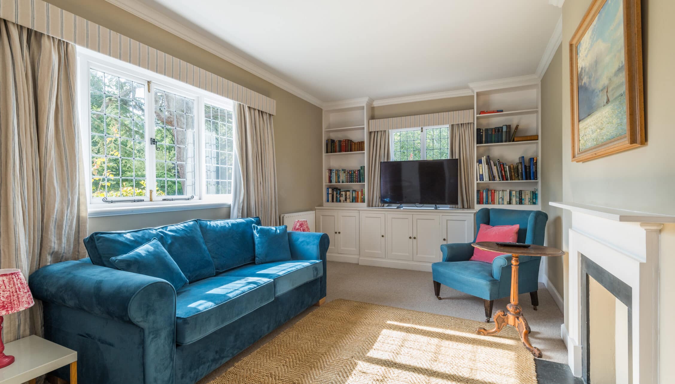 Nedging Hall, Suffolk – Sitting room with blue velvet sofa, built-in shelving, and large bay windows.