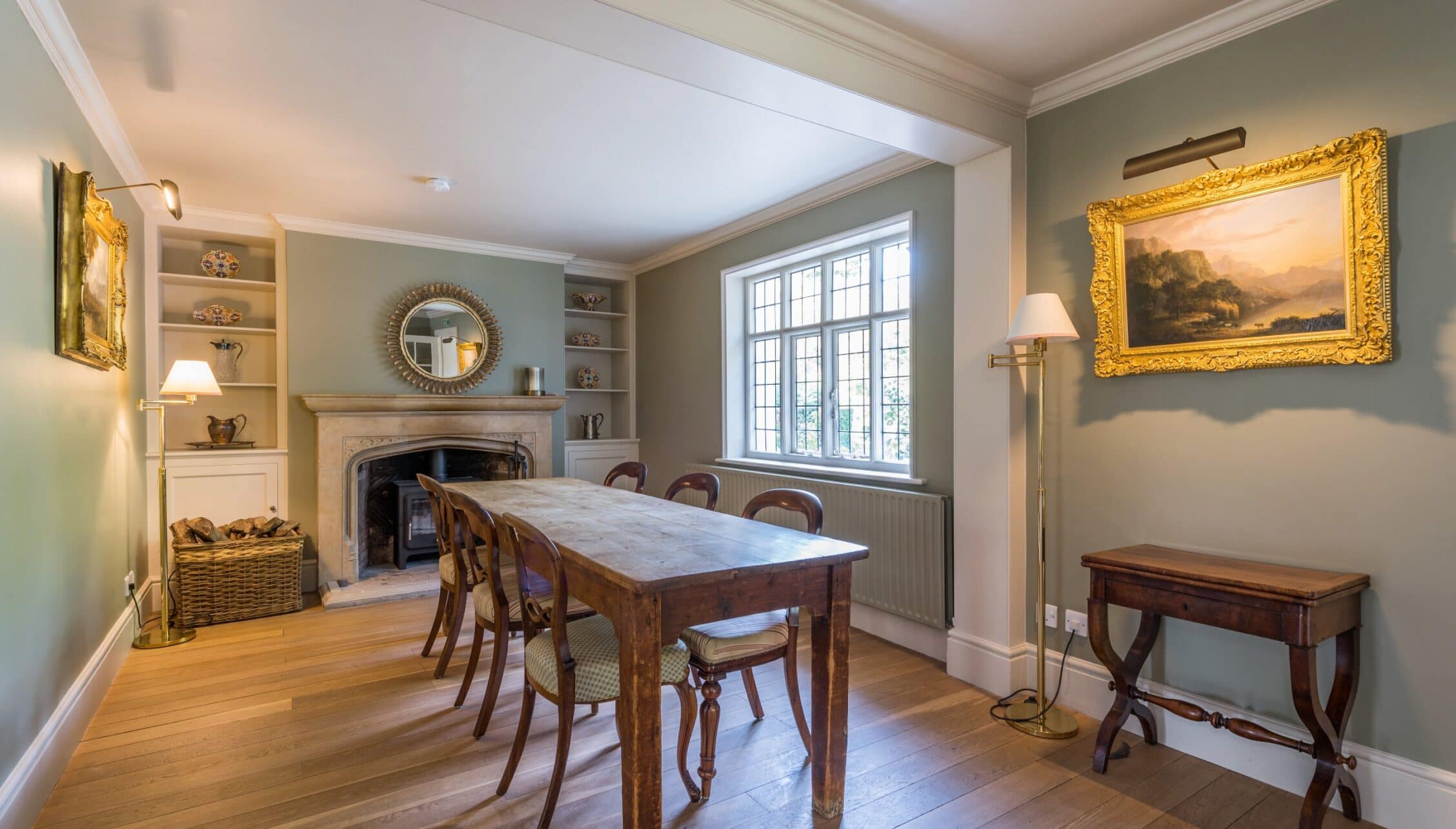 Nedging Hall, Suffolk – Formal dining room with wooden table, fireplace and gilt-framed landscape painting.