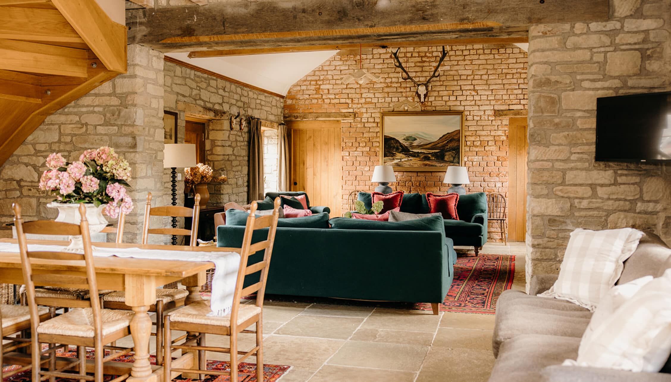 The Barns – Exclusive Hire, Herefordshire – Open-plan living space with exposed stone walls, wooden beams, and green upholstered sofa.