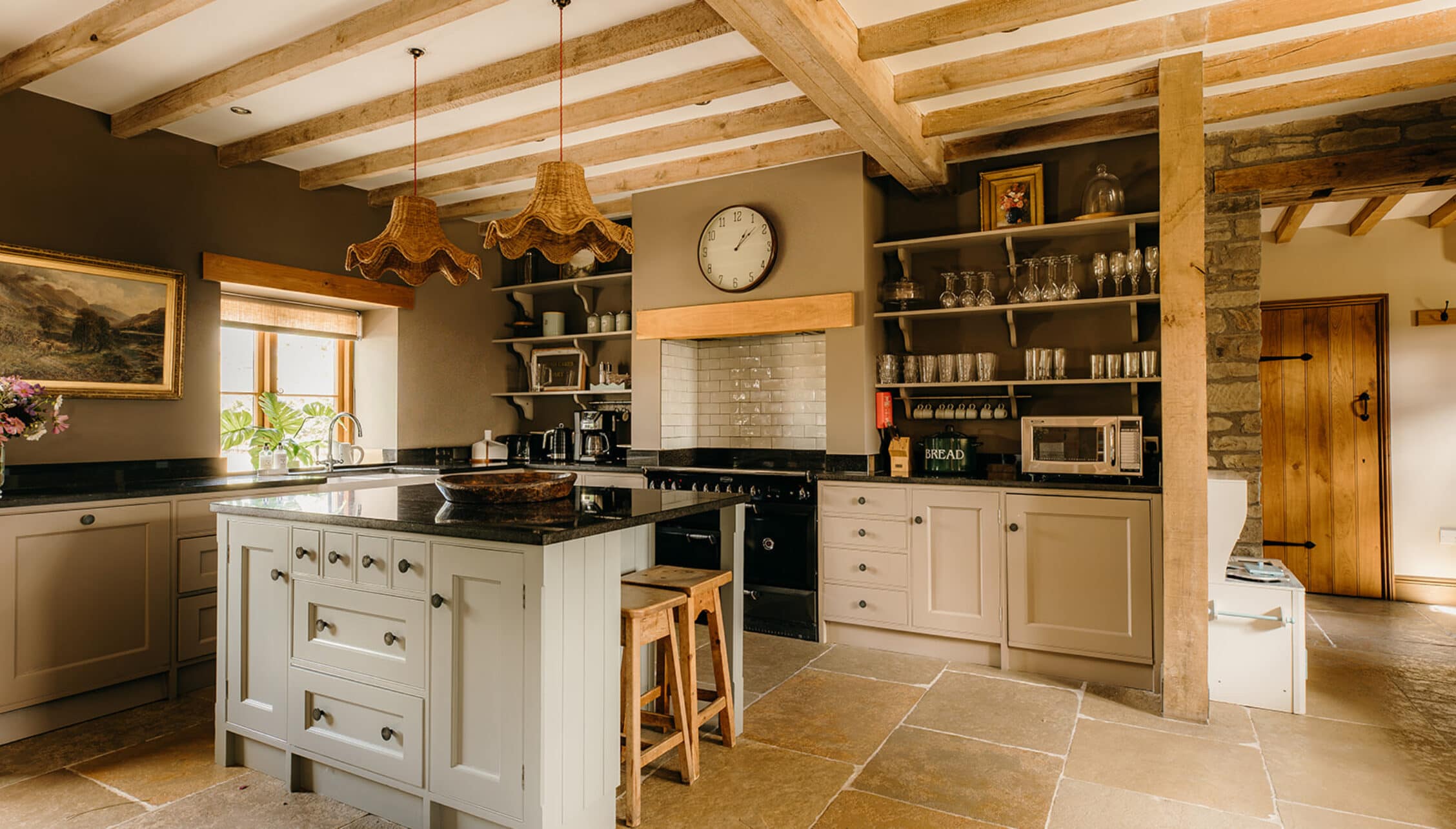 The Barns – Exclusive Hire, Herefordshire – Kitchen with exposed wooden beams, cream cabinetry, and black Aga cooker.