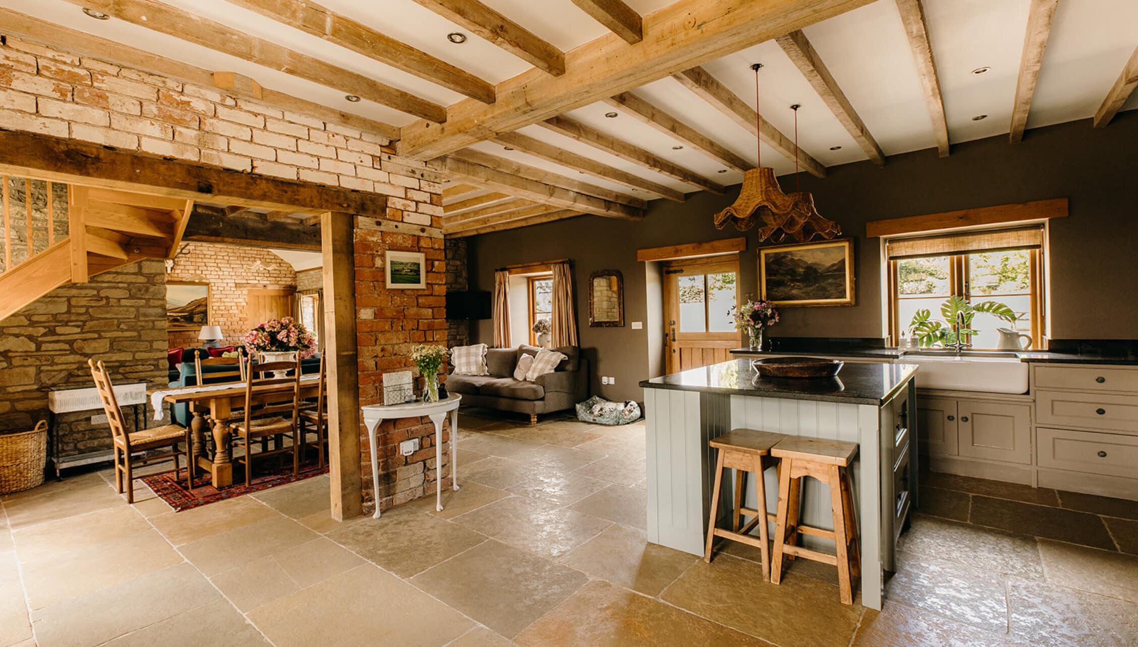 The Barns – Exclusive Hire, Herefordshire – Open-plan kitchen and living area with exposed timber beams and brick fireplace.