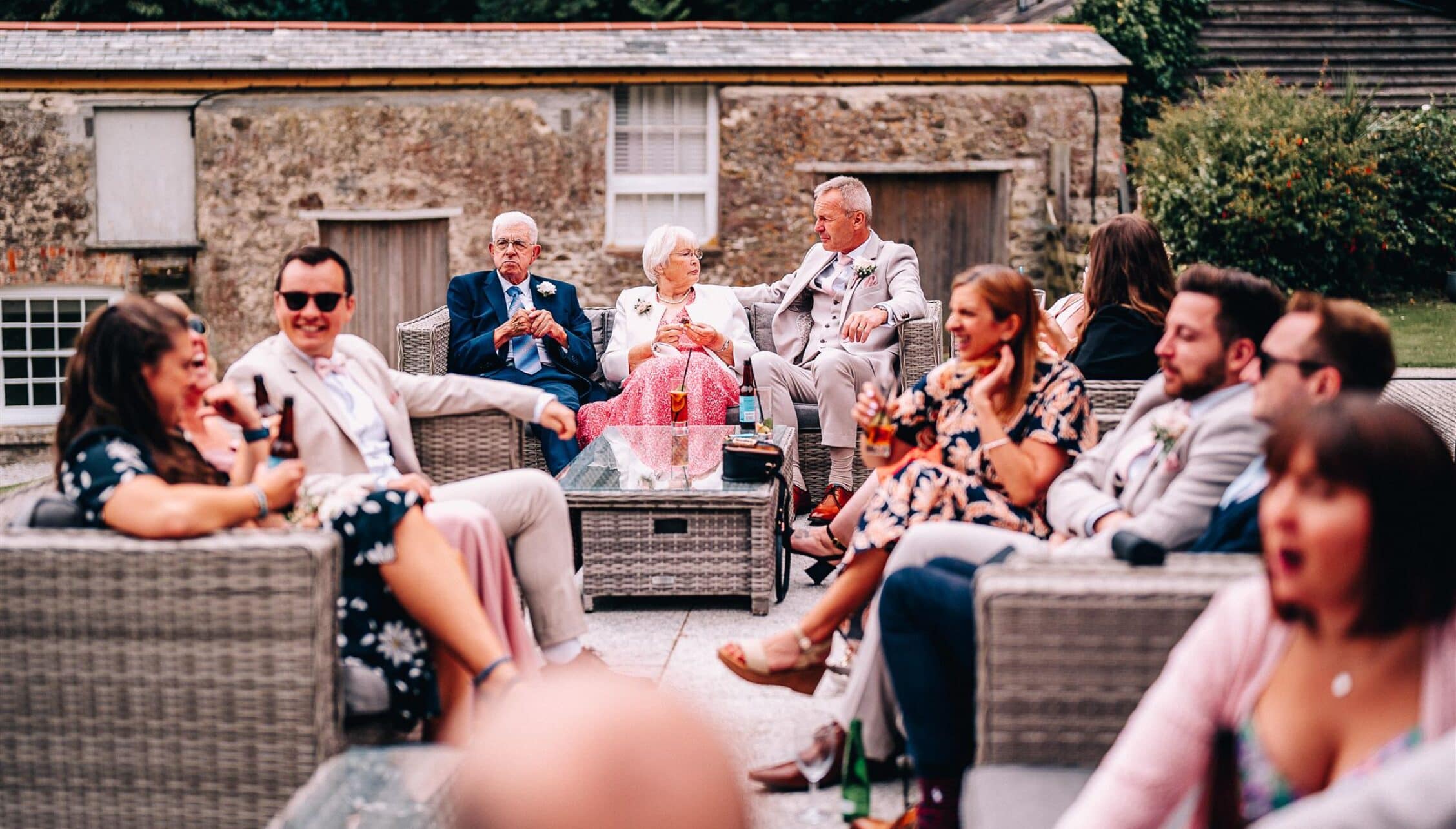 Tredudwell Manor, Cornwall – Wedding guests seated on patio furniture in front of stone cottage.