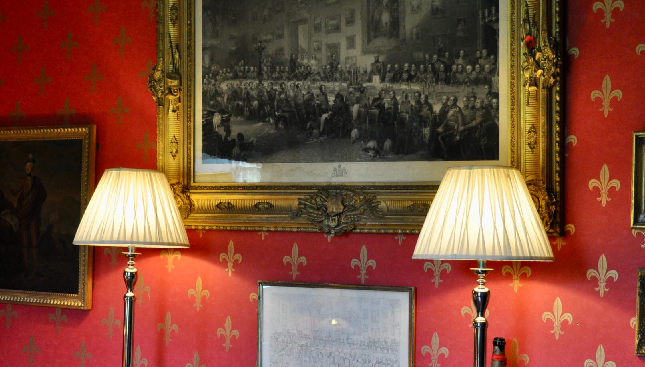 Wardhill Castle, Aberdeenshire – Red damask room with gold-framed historical engraving and pleated lamp shades.
