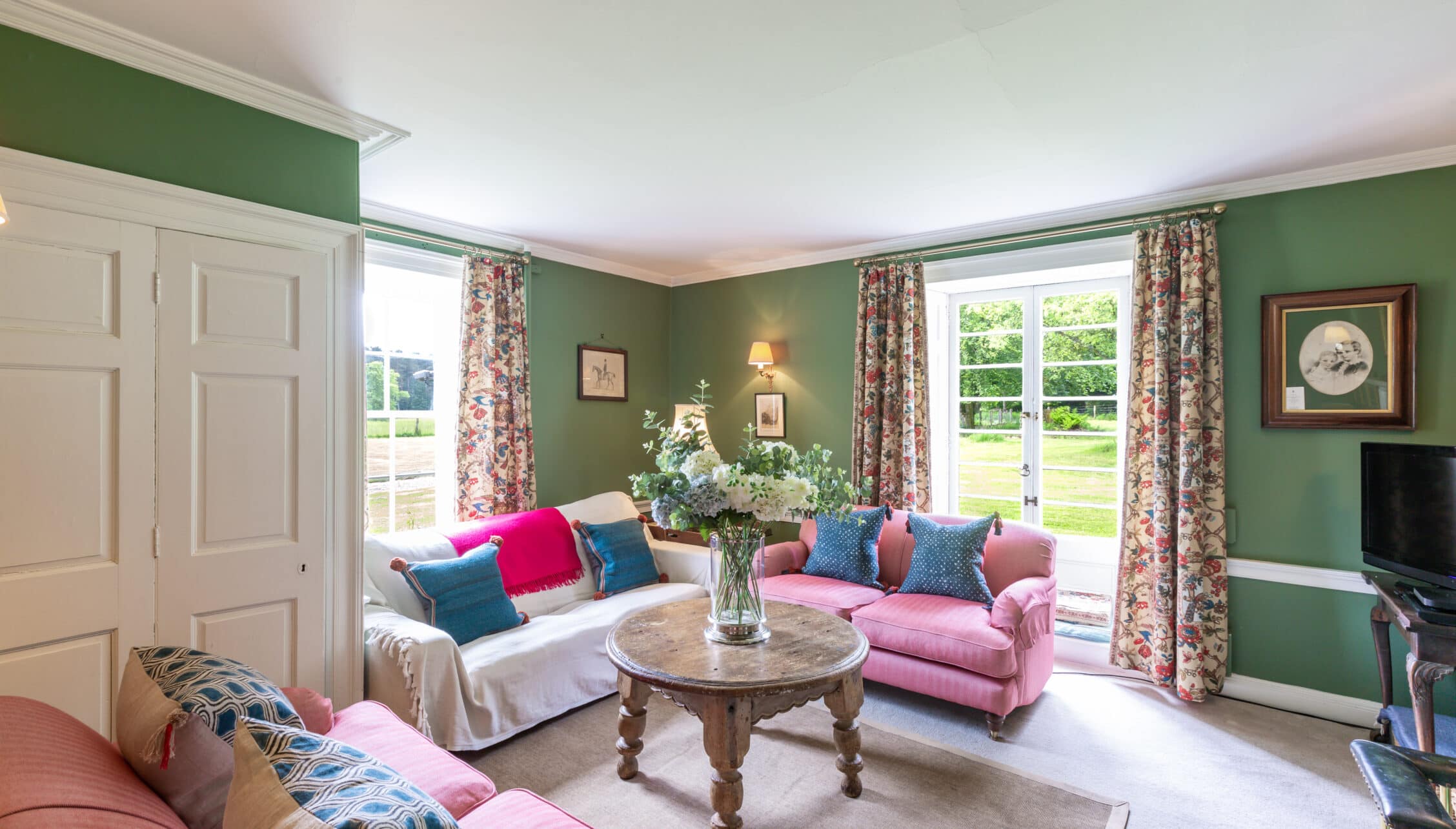 Wardhill Castle, Aberdeenshire – Green sitting room with pink armchair, floral curtains and French doors to garden.