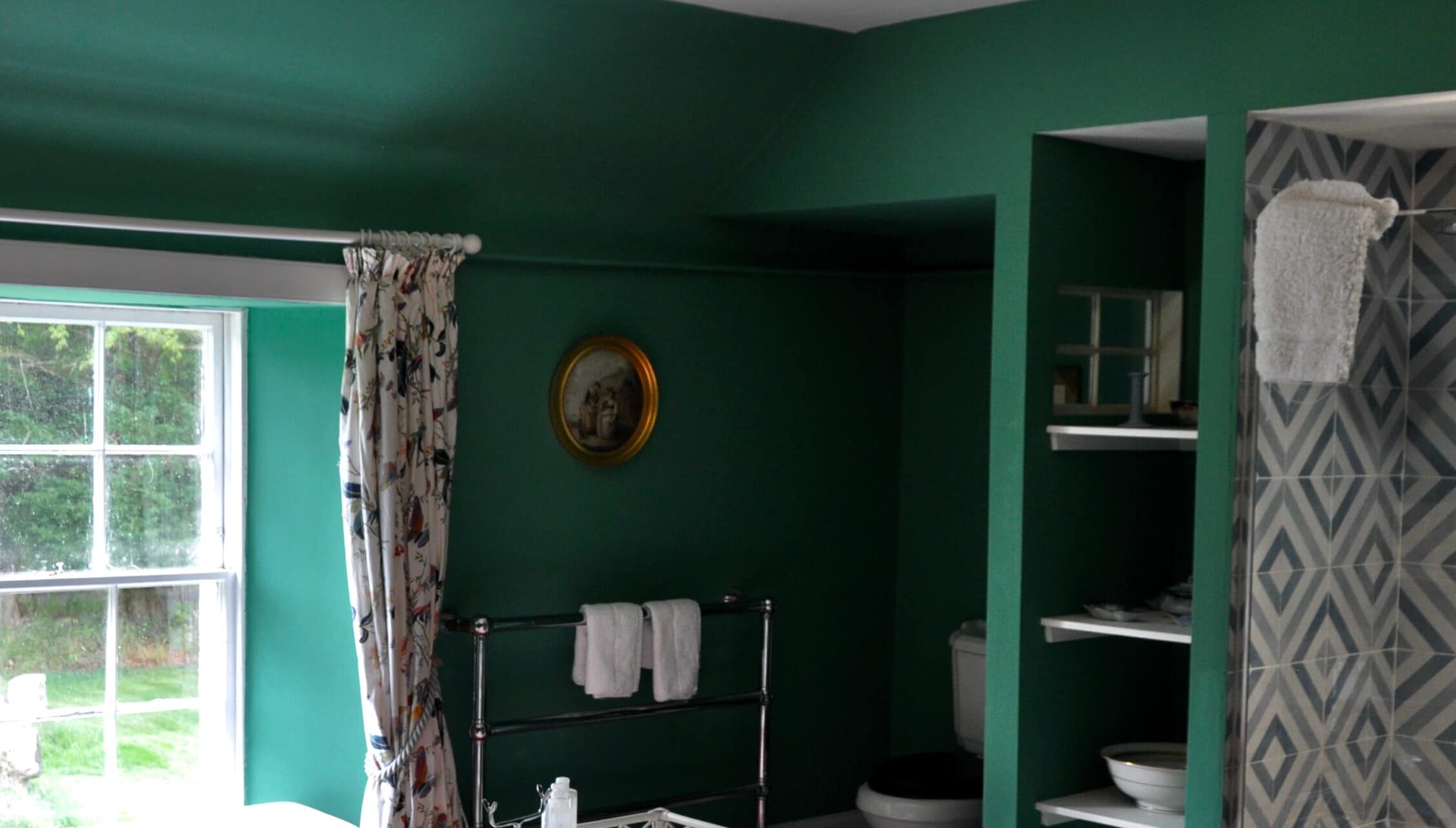 Wardhill Castle, Aberdeenshire – Bedroom with emerald green walls, metal bed frame, and ensuite bathroom with shelving.