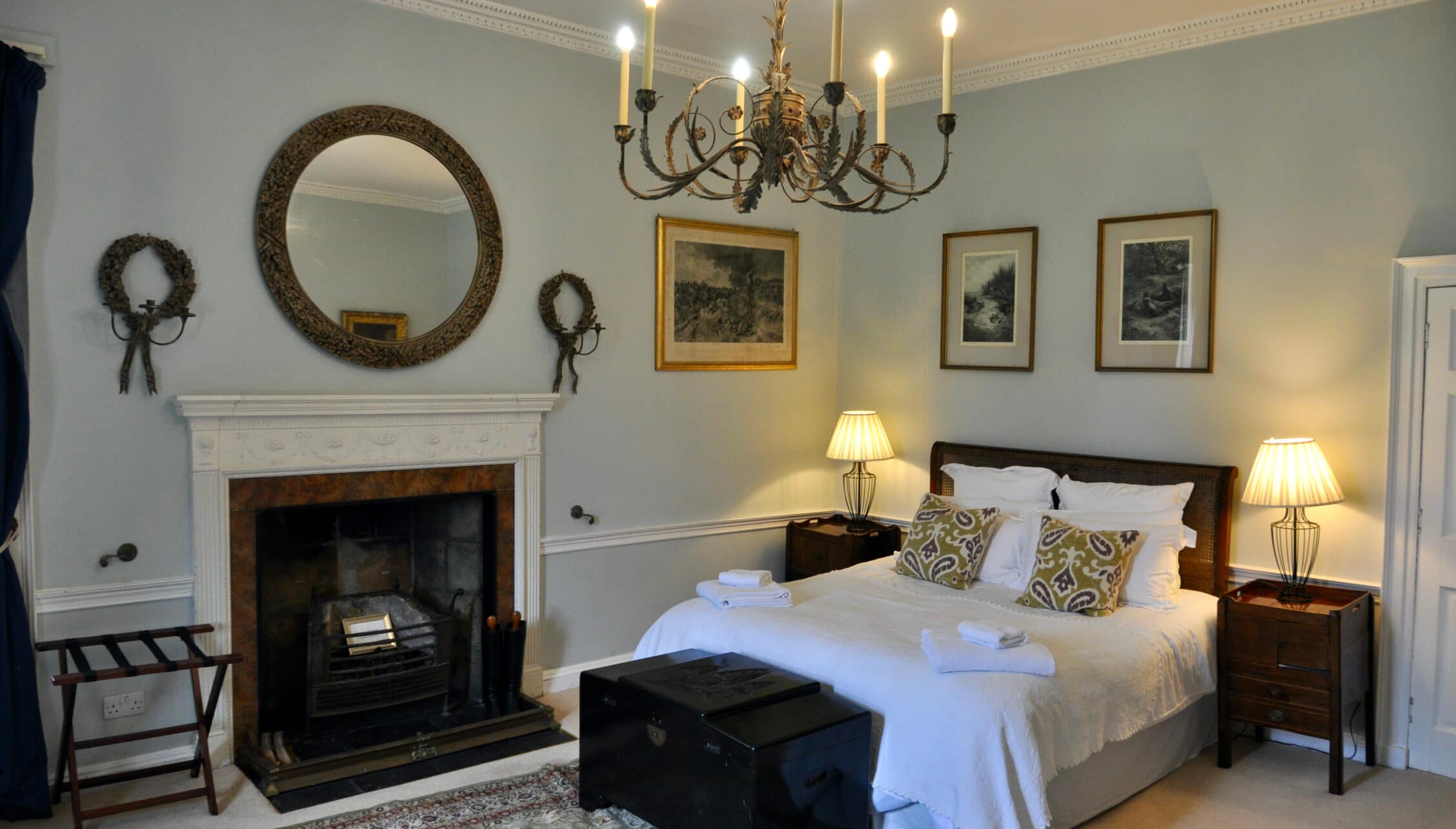 Wardhill Castle, Aberdeenshire – Bedroom with fireplace, brass chandelier, and wood-framed bed with white linens.