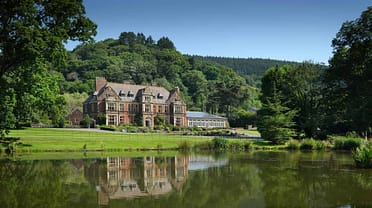 Knowle Manor – Victorian mansion with red brick façade and mansard roof beside tree-lined lake.