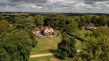 Nedging Hall, Suffolk – Aerial view of red-brick country house with manicured lawns and mature woodland surrounding.