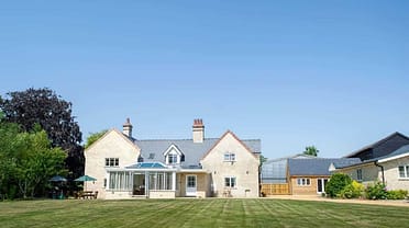Stow Manor, Suffolk – Stone country house with slate roof and modern glass extension, viewed from manicured lawn.