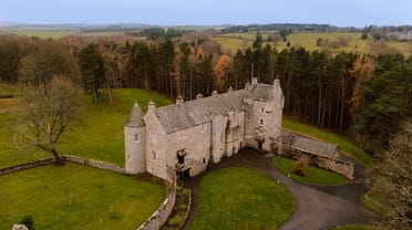 Ferniehirst Castle, East Lothian – Stone castle with conical towers surrounded by woodland and rolling farmland.