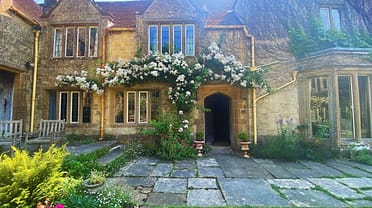 Symondsbury Manor, Dorset – Stone courtyard with white climbing roses over arched entrance doorway.