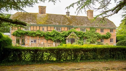 The Long House – Red brick country house with leaded windows and tall chimneys, surrounded by mature hedging.