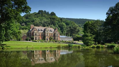 Knowle Manor – Victorian mansion with red brick façade and mansard roof beside tree-lined lake.