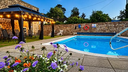 Brookside, Herefordshire – Swimming pool with stone boundary wall, lit pergola, and purple flowers.