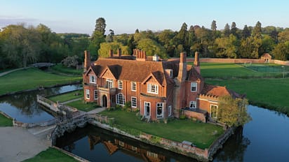 Boxted Hall, Suffolk – Red brick country house with tall chimneys beside moat and bridge.