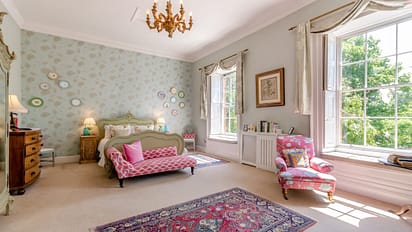 Breedon Hall, Leicestershire – Spacious bedroom with sage-green four-poster bed, patterned wallpaper, and large sash windows.
