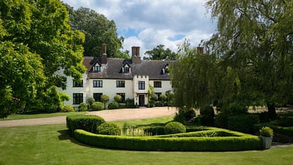 Hill House Norfolk, Norfolk – Cream-rendered country house with black gable windows, brick chimneys, gravel drive, and manicured grounds with topiary hedges.