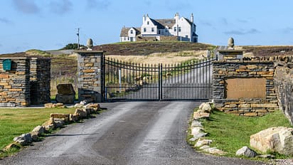 House of the Northern Gate, Highland – White stone country house on moorland hillside with black iron gates and stone gateposts.