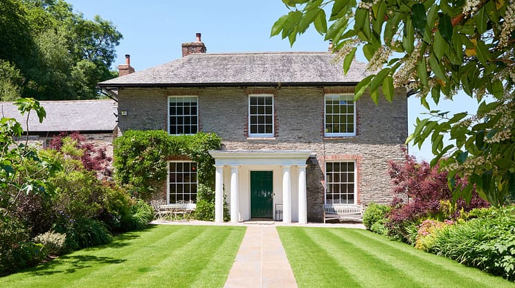 Gitcombe House, Devon – Stone Georgian house with white portico, manicured lawn, and flowering shrubs.